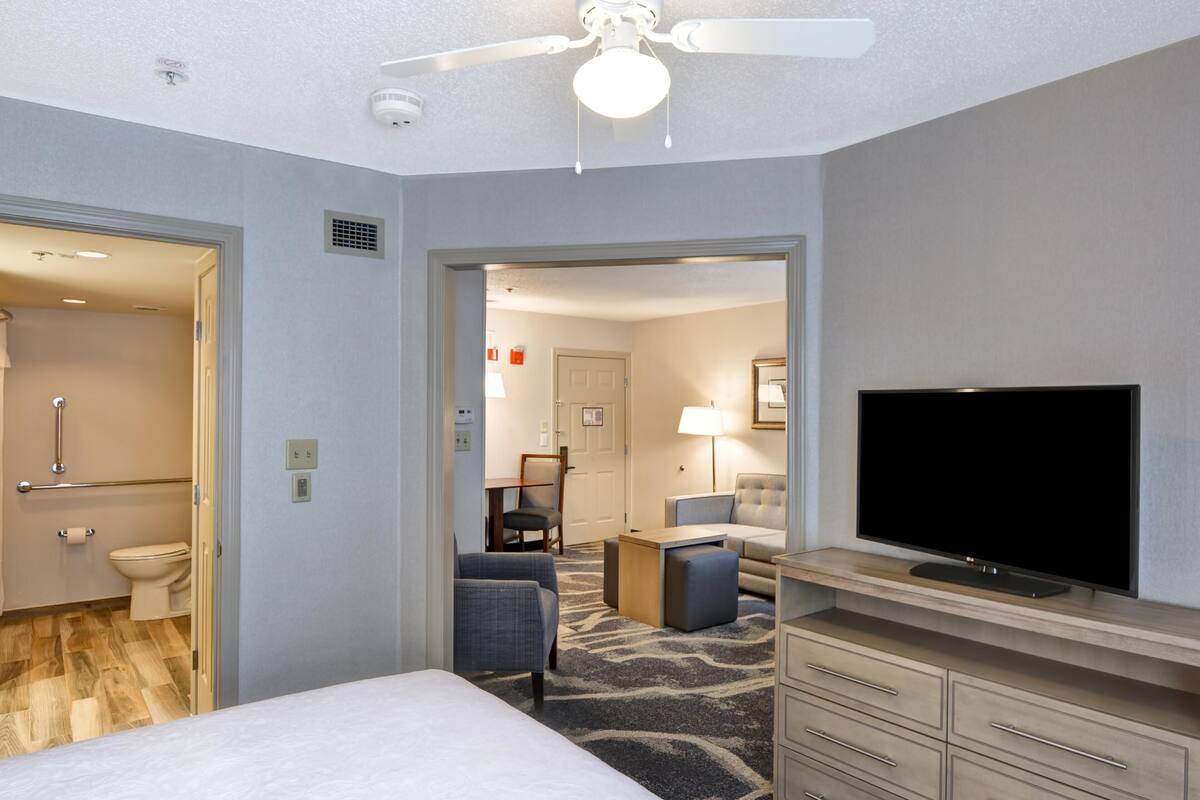 Habitación de hotel con cama, televisión, escritorio, silla, lámpara y baño.