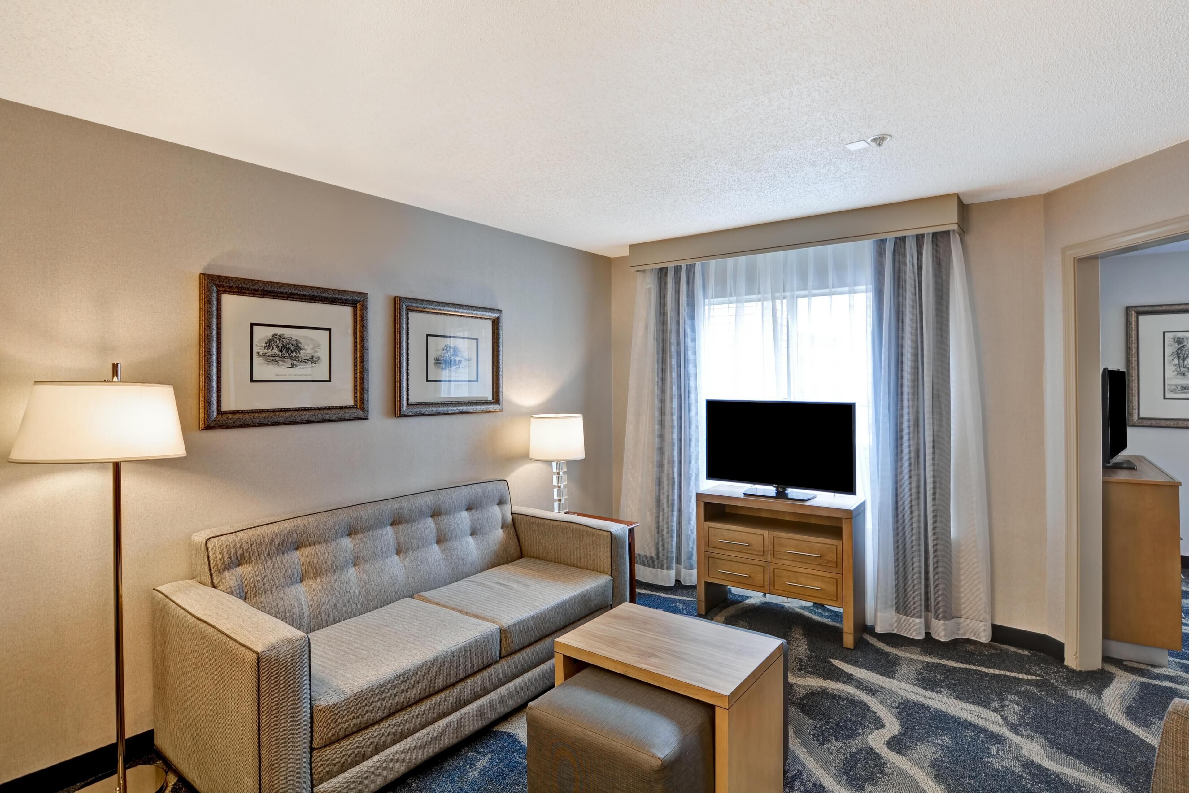 A hotel room with a sofa, a small table, a TV, a desk, and two framed pictures on the wall.