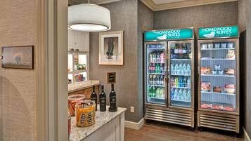 Una suite hotel con un minibar, un cartello per il negozio della suite e due frigoriferi Homewood Suites forniti di bevande e snack.