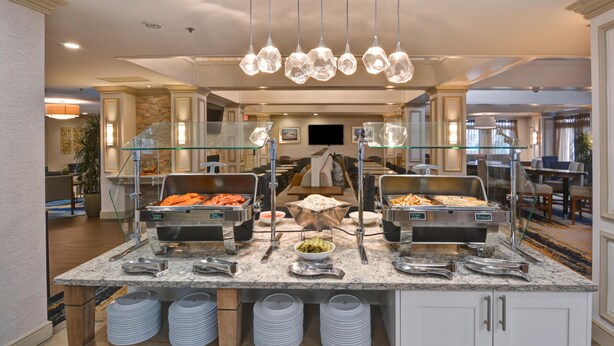 Een buffetopstelling met diverse gerechten, een glazen scheiding en een moderne kroonluchter.