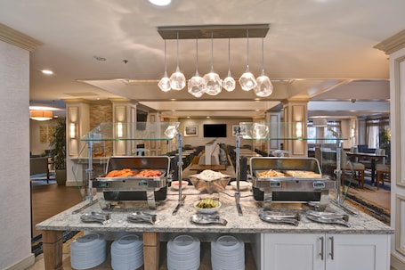 A buffet setup with various food options, a glass partition, and a modern chandelier.