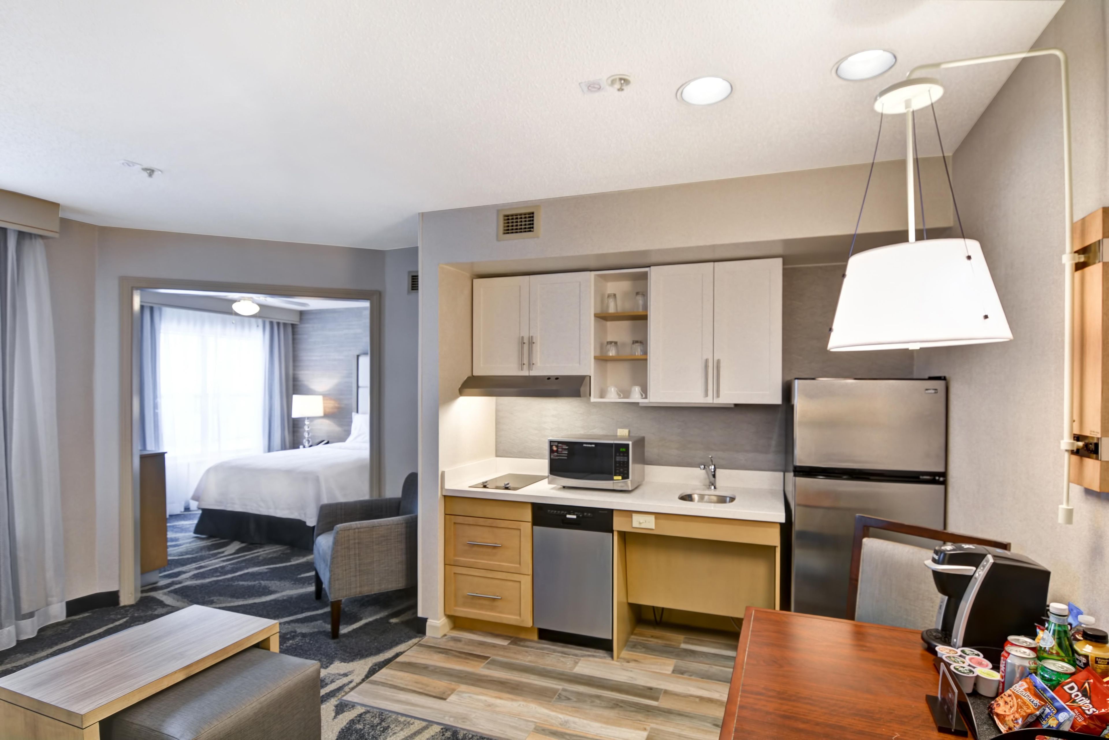 A modern hotel room with a kitchenette, a dining area, and a separate bedroom.