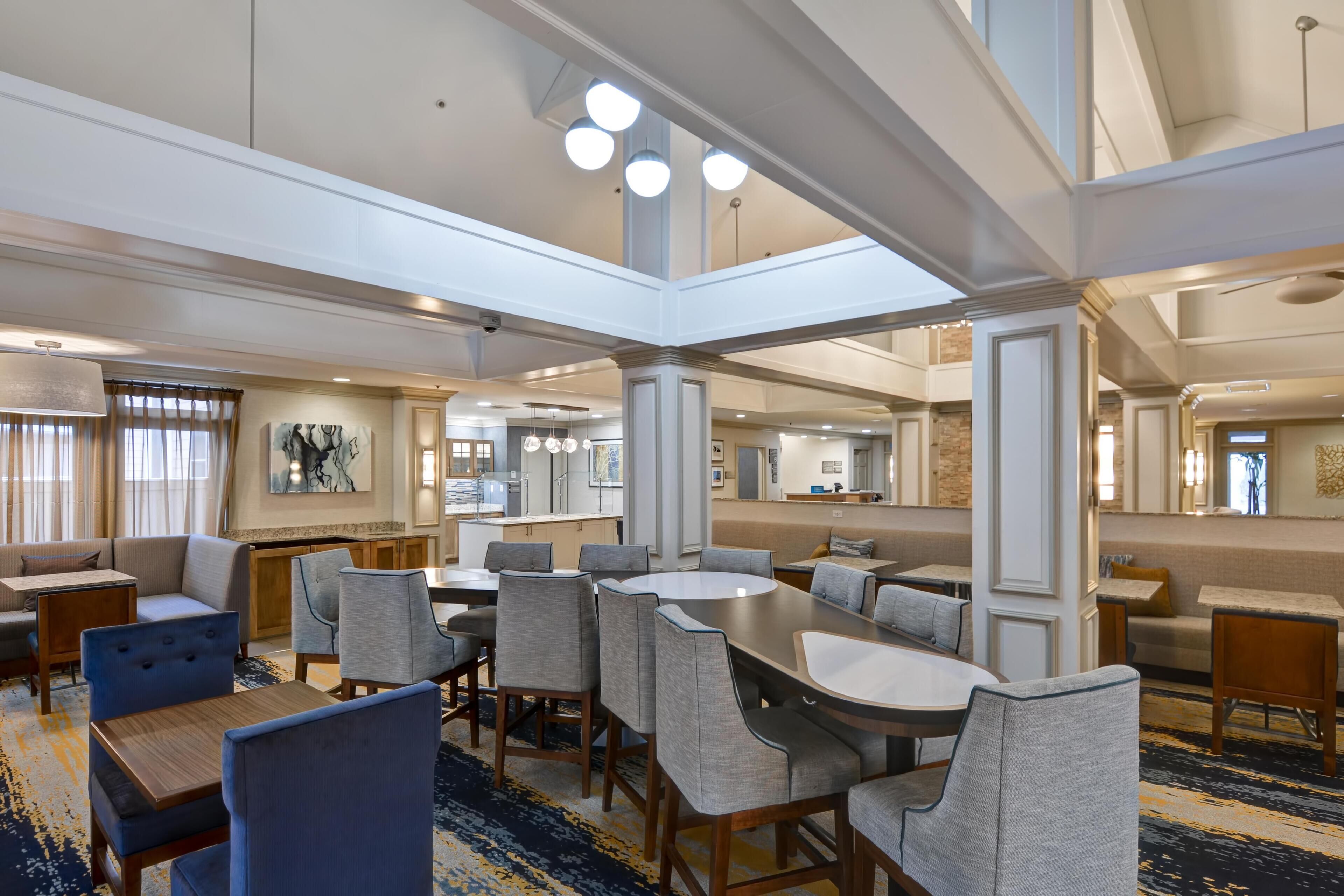 Un amplio vestíbulo de hotel con techos altos, varias zonas de estar y una mesa de comedor central.