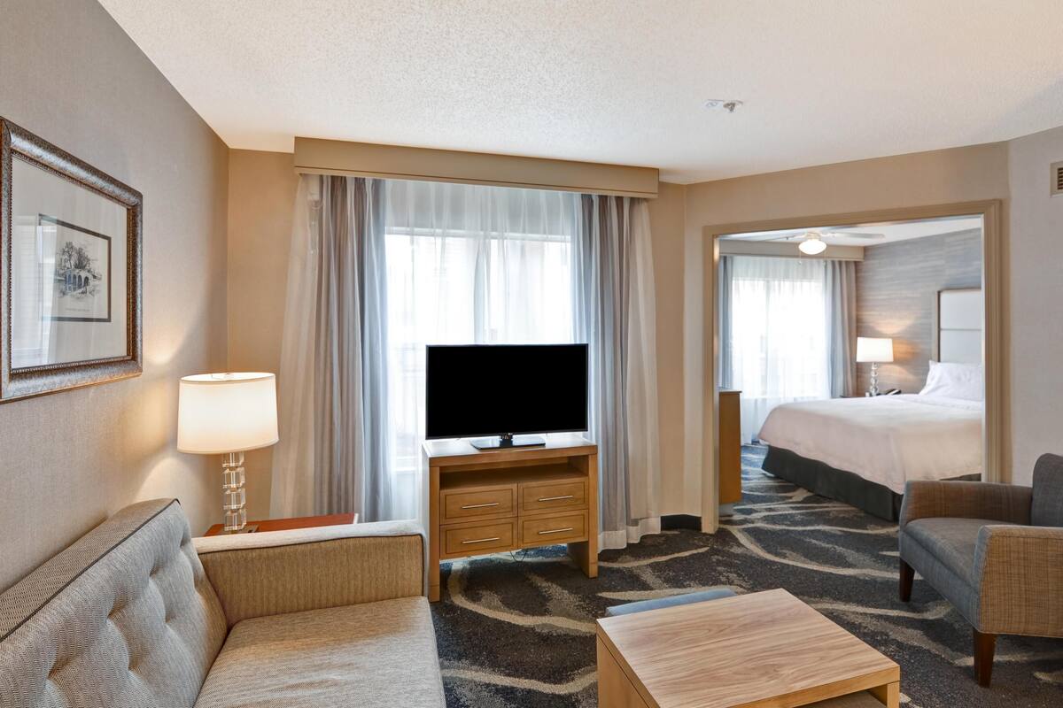 Habitación de hotel con televisor de pantalla plana, sofá, mesa de centro, cama y escritorio con lámpara.