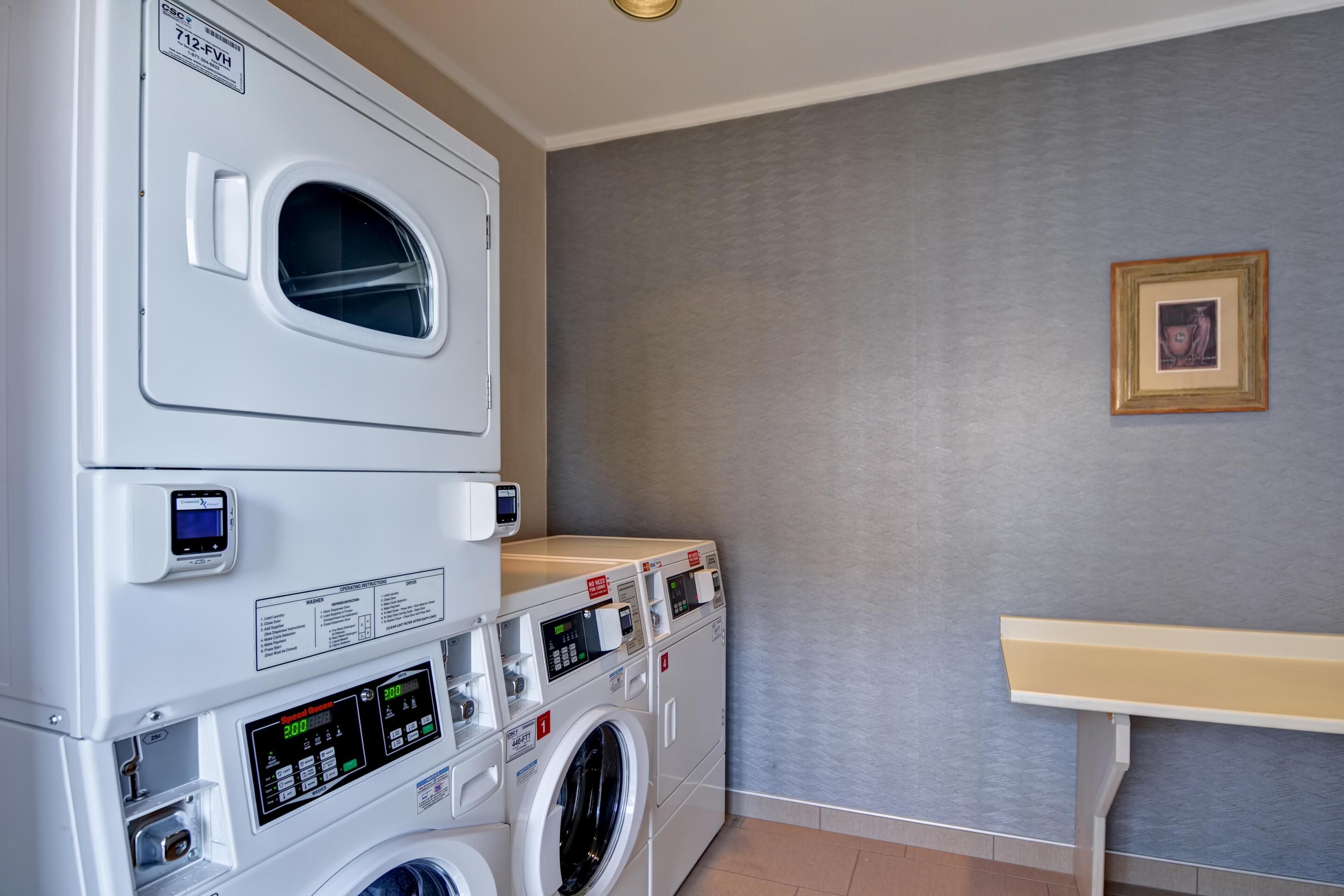 A laundry room with stacked washers and dryers, a control panel, and a small table.