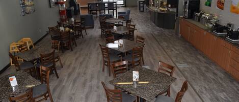 A spacious dining area with multiple tables and chairs, a kitchen area with appliances, and a view of the outside.