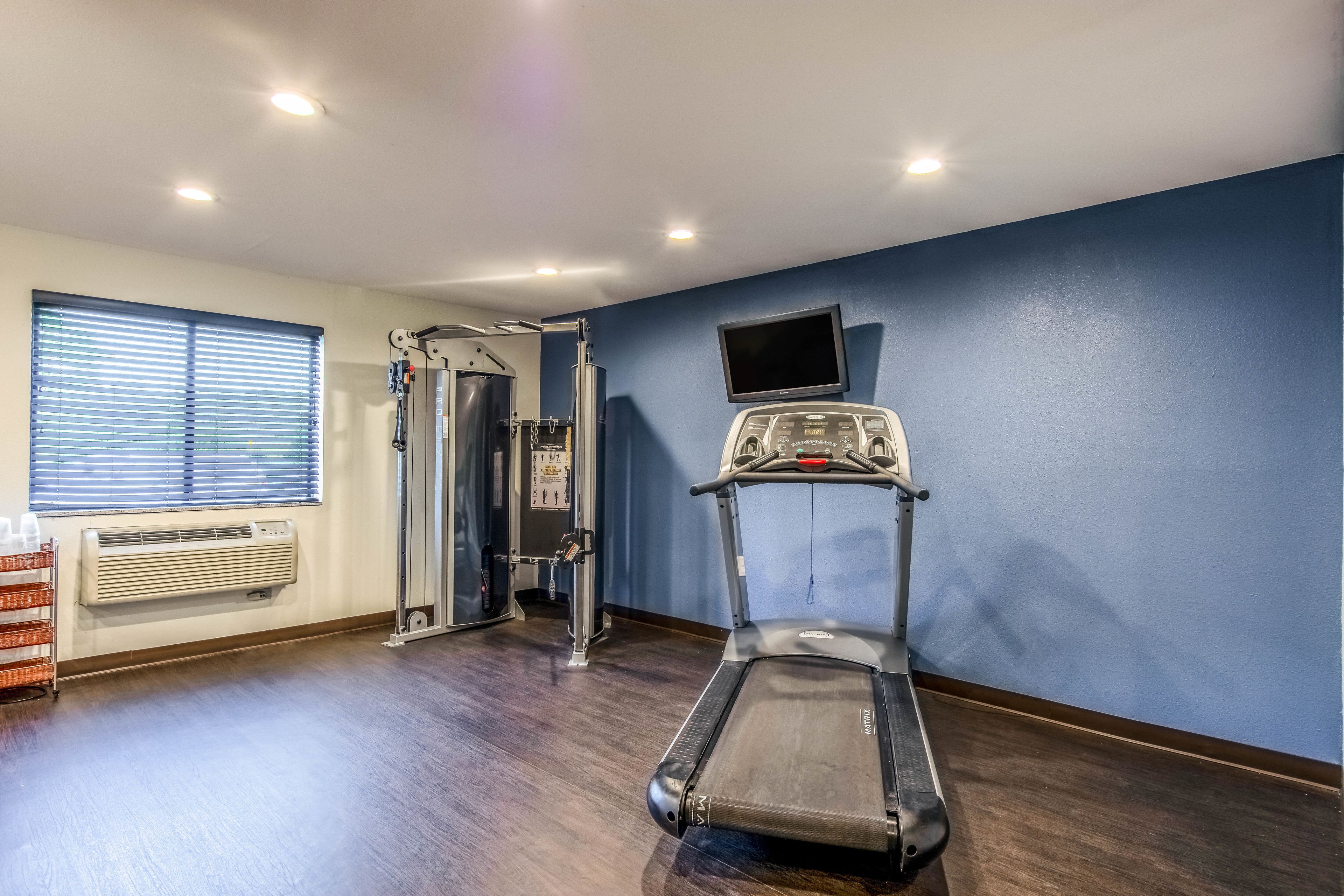 Een fitnessruimte met een loopband, krachtapparaten en een televisie aan de muur.