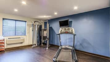 Een fitnessruimte met een loopband, krachtapparaten en een televisie aan de muur.