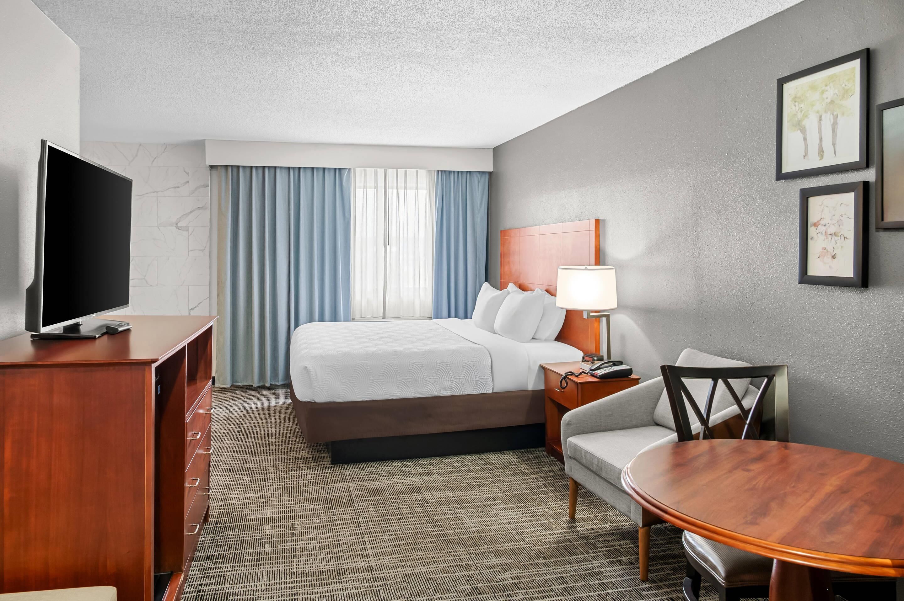 A hotel room with a bed, a TV, a desk, a chair, and a table.