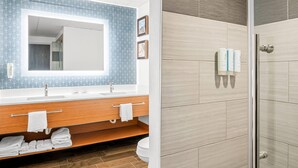 A bathroom with a large mirror, wooden vanity, and a shower area.