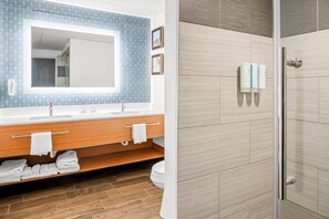 A bathroom with a large mirror, wooden vanity, and a shower area.