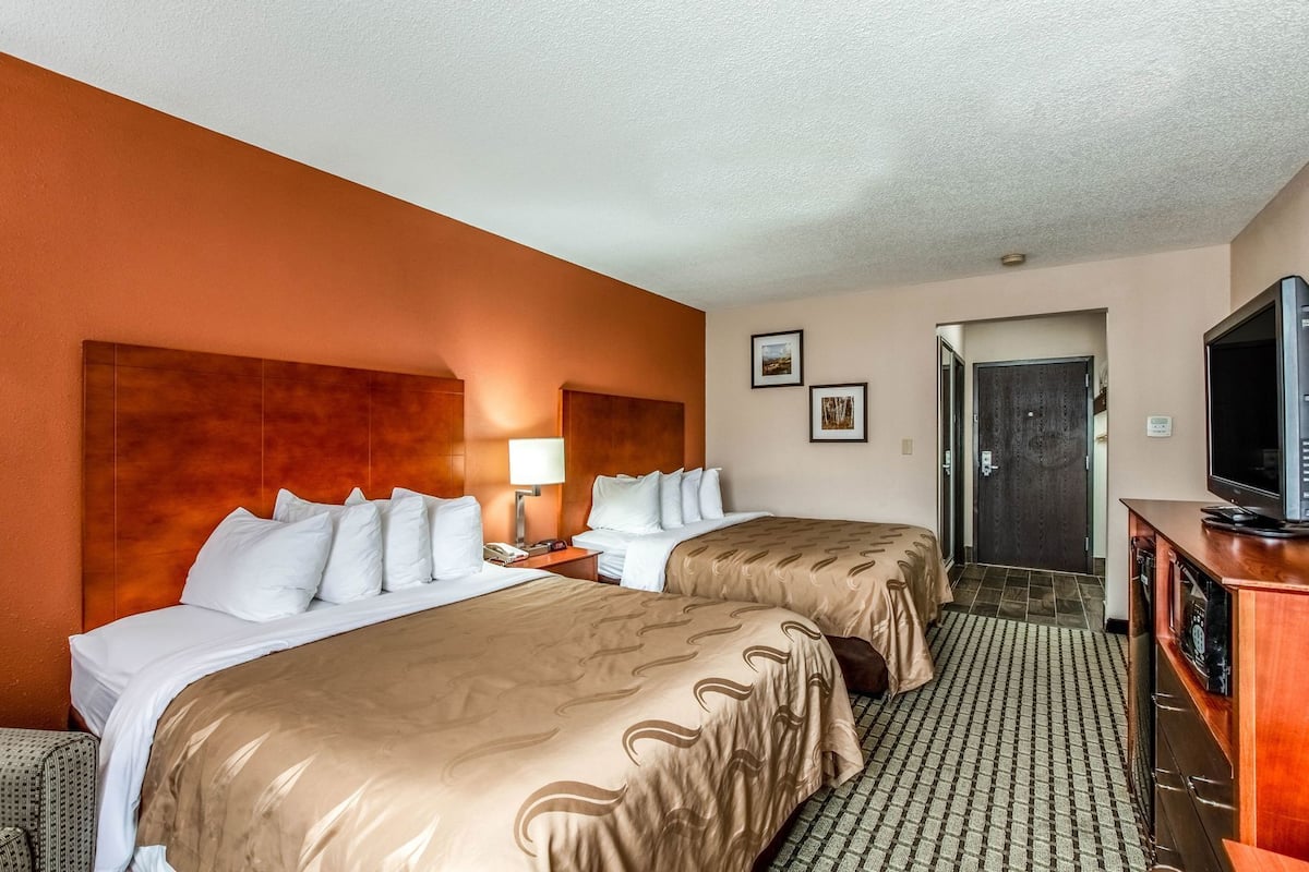 Une chambre d’hôtel avec deux lits, une télévision, un bureau et une porte donnant sur une autre pièce.