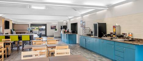 A modern kitchen with blue cabinets, wooden tables, and chairs.