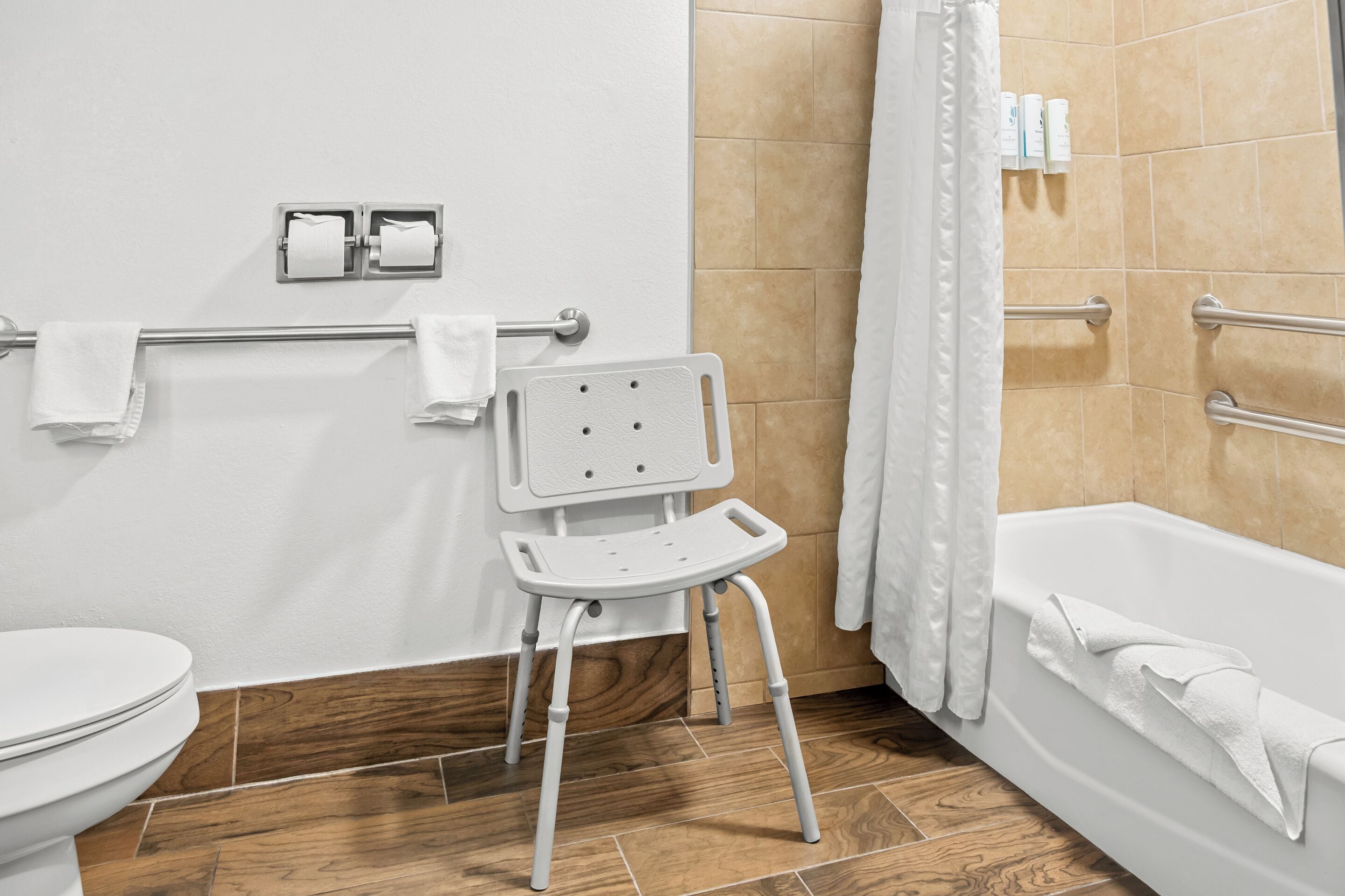 A bathroom with a white toilet, a white bathtub with a towel, a white shower curtain, and a white grab bar.