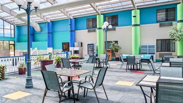 An indoor dining area with tables and chairs, a glass ceiling, and potted plants.