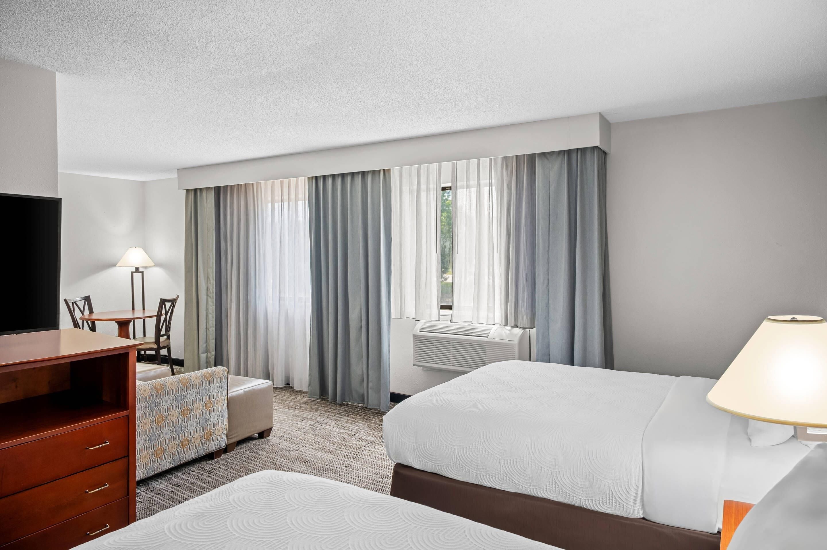 Ein Hotelzimmer mit Bett, Schreibtisch, Stuhl, Fernseher und einem Fenster mit Vorhängen.