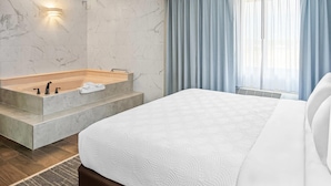 A modern hotel room with a large bed, a built-in bathtub, and a large window with curtains. - Country Inn & Suites by Radisson, Muskegon, MI (Muskegon)