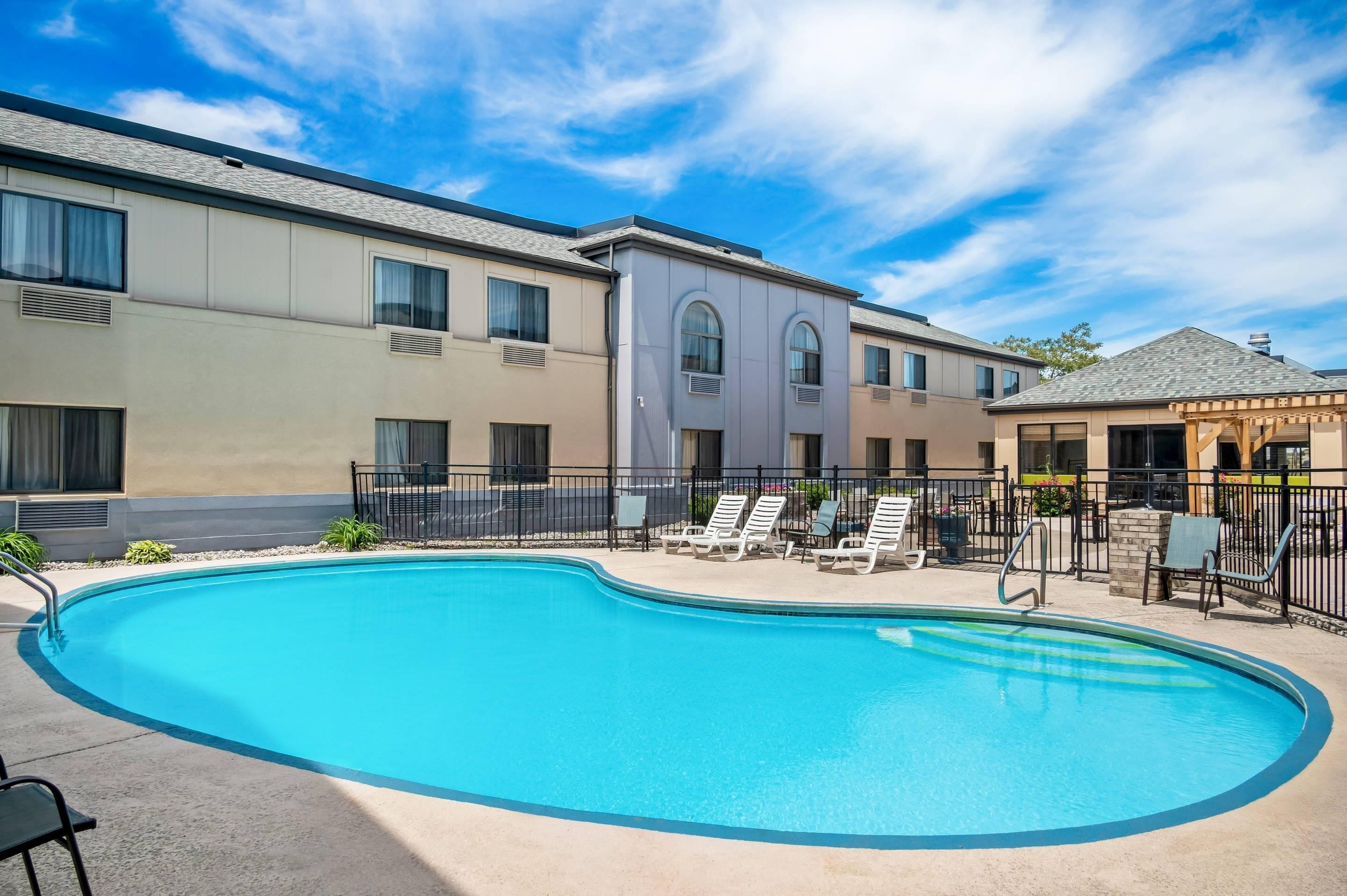 A swimming pool with lounge chairs, a covered patio, and a building with multiple windows and a flat roof.