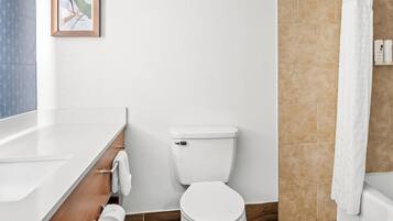 Et moderne badeværelse med et hvidt toilet, en trækommode, et billede i ramme på væggen og en brusevæg.