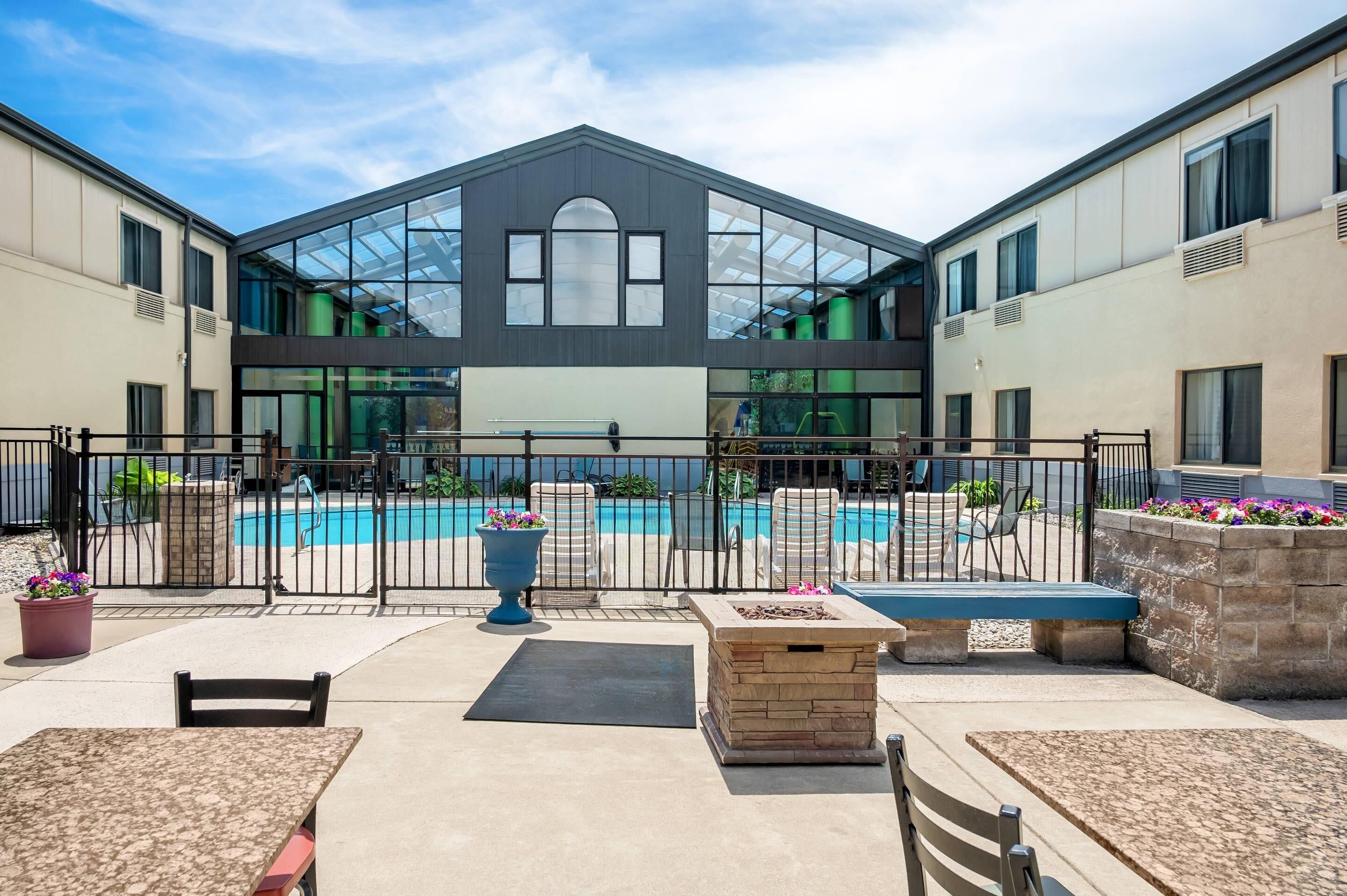 A modern building with a glass facade, a swimming pool, outdoor seating, and a stone fire feature.
