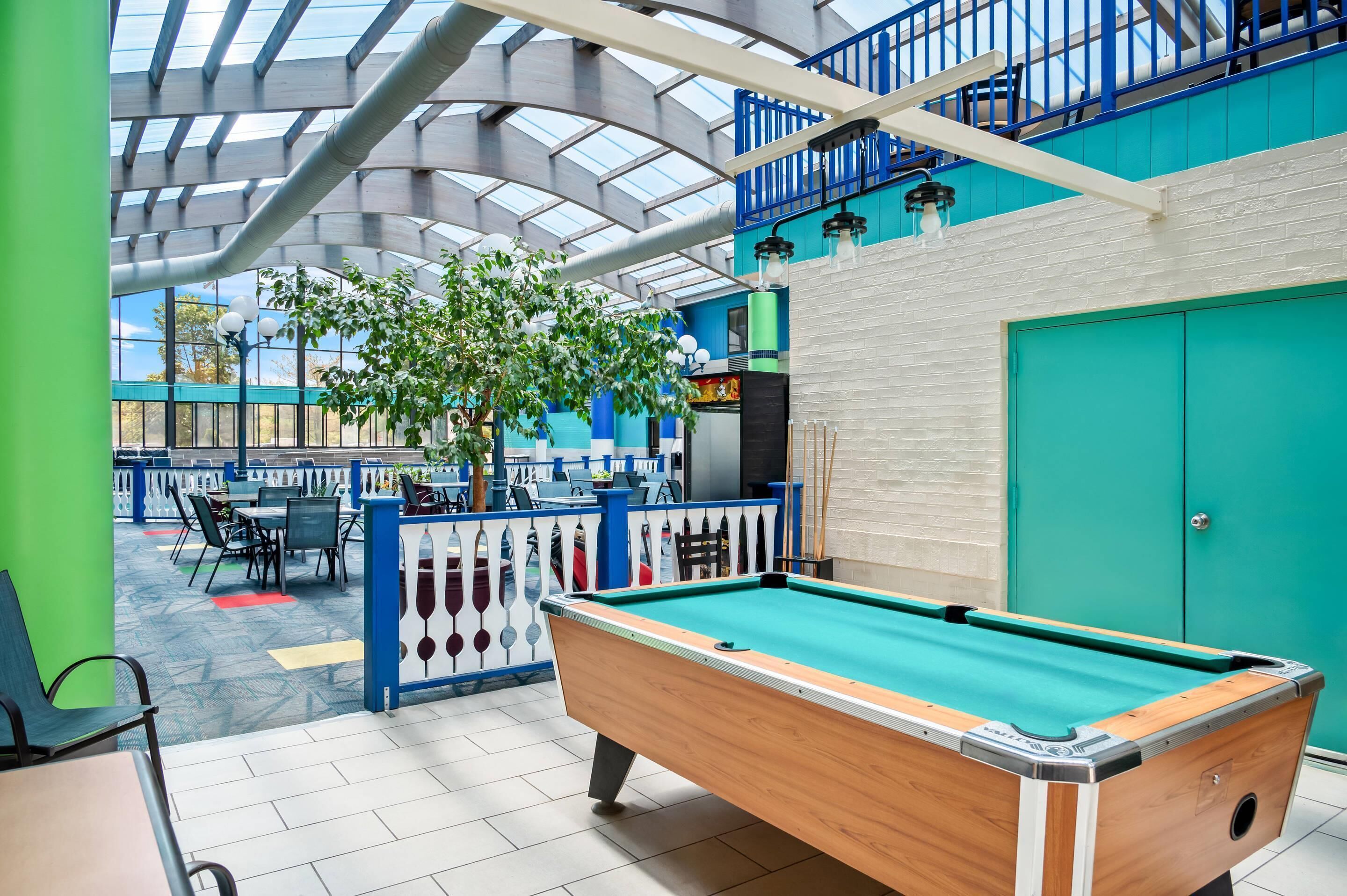 An indoor pool table with a green felt surface, surrounded by a white and blue railing, and a blue door in the background.