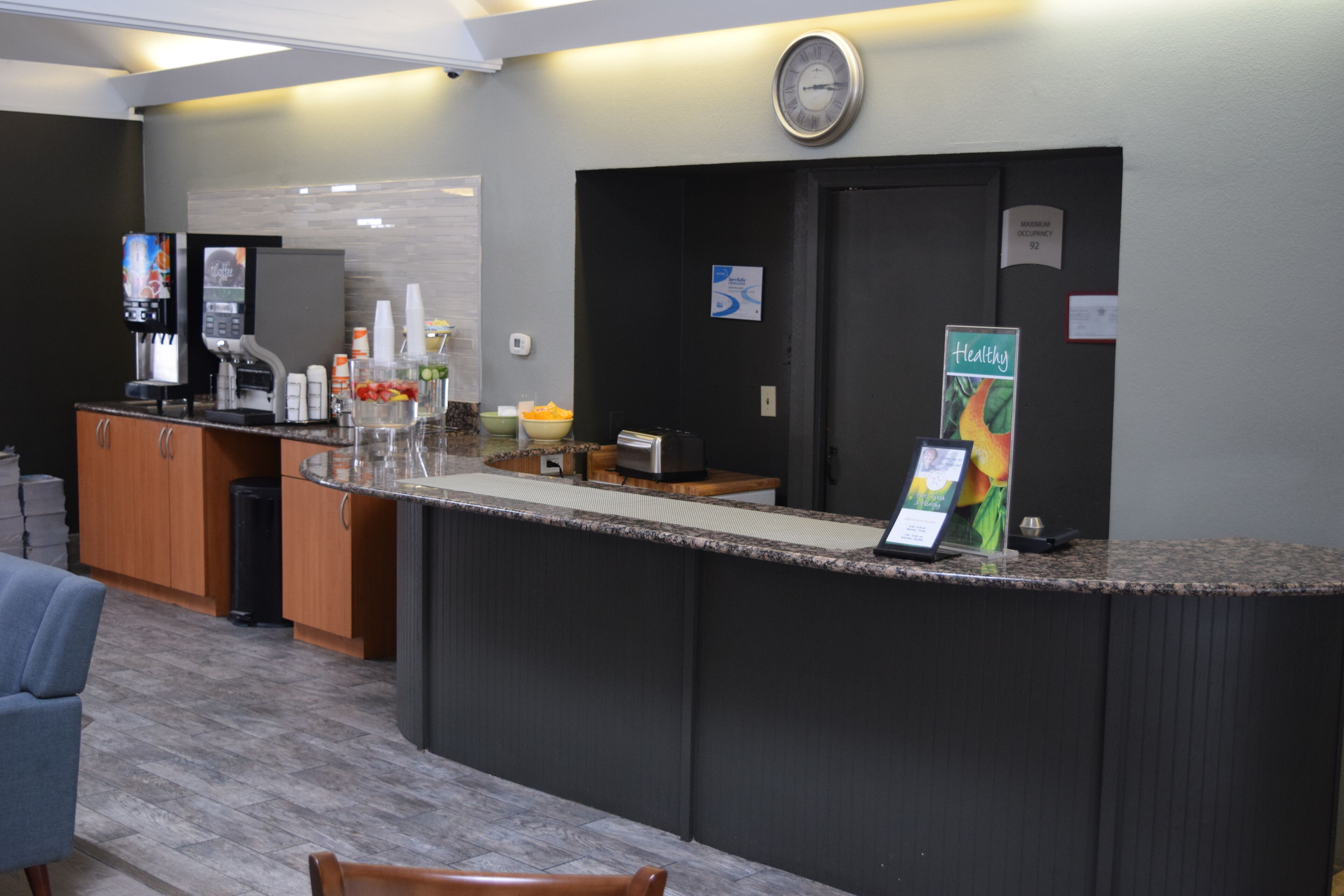 A hotel reception area with a counter, coffee machine, and a clock on the wall.