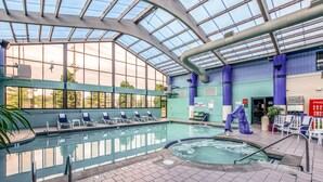 An indoor swimming pool with lounge chairs and a hot tub area.