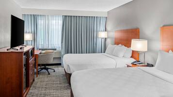 A hotel room with two beds, a desk, a TV, and a lamp.