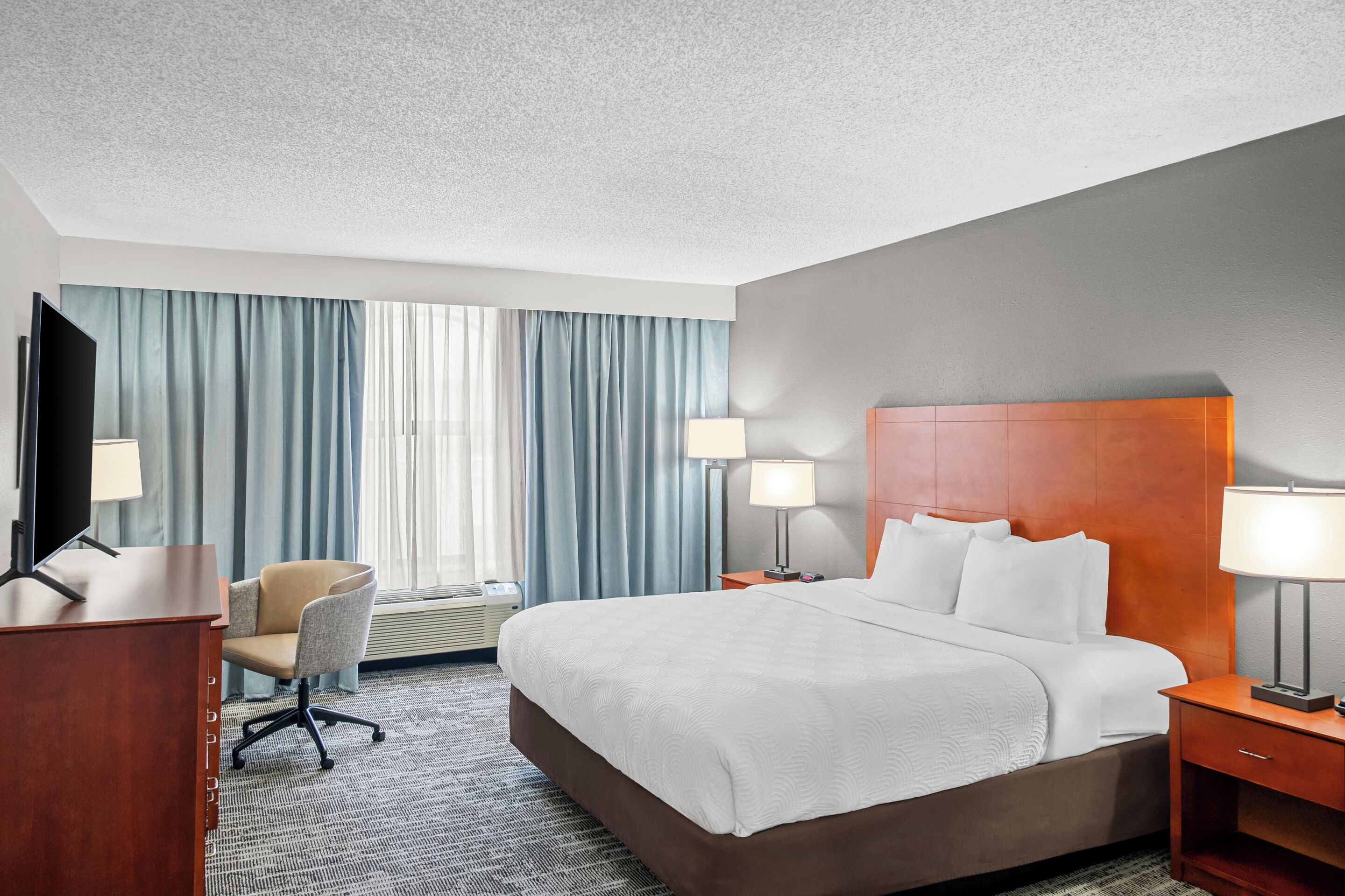 A hotel room with a large bed, two bedside tables with lamps, a desk with a chair, and a flat-screen TV.