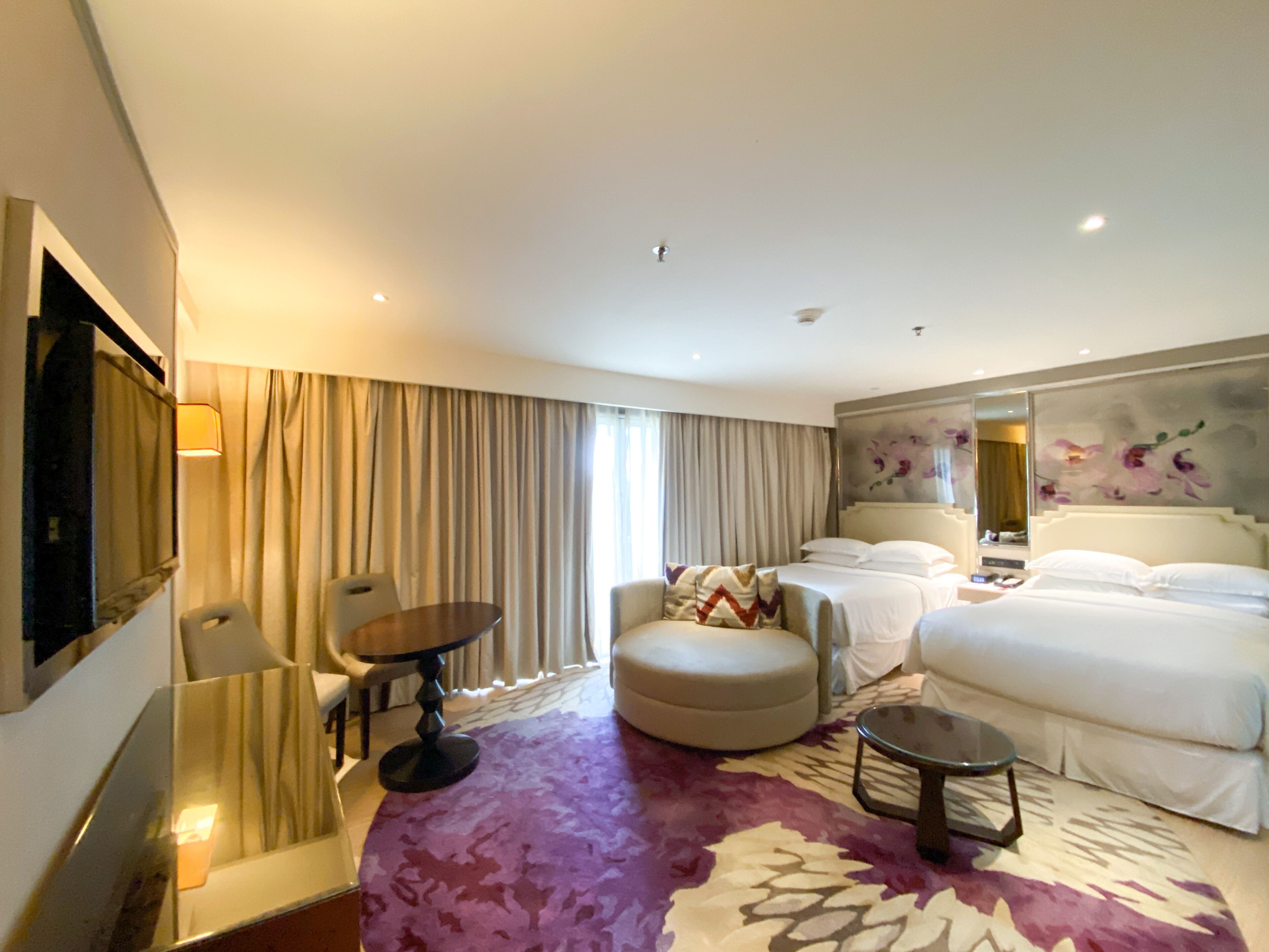 Una habitación de hotel con una cama, un sofá, una mesita, una silla y un espejo grande.