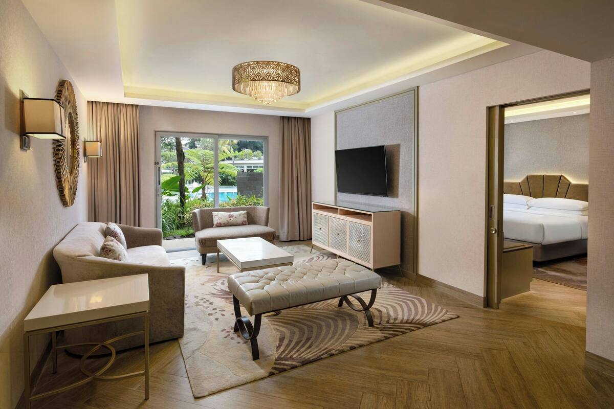 Une chambre d’hôtel moderne équipée d’un canapé, d’un pouf, d’une table basse et d’un téléviseur fixé au mur.