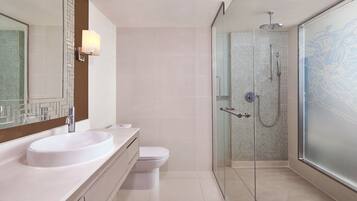 Un baño moderno con un espejo grande, un lavamanos blanco, un inodoro y una zona de ducha con mampara de vidrio.