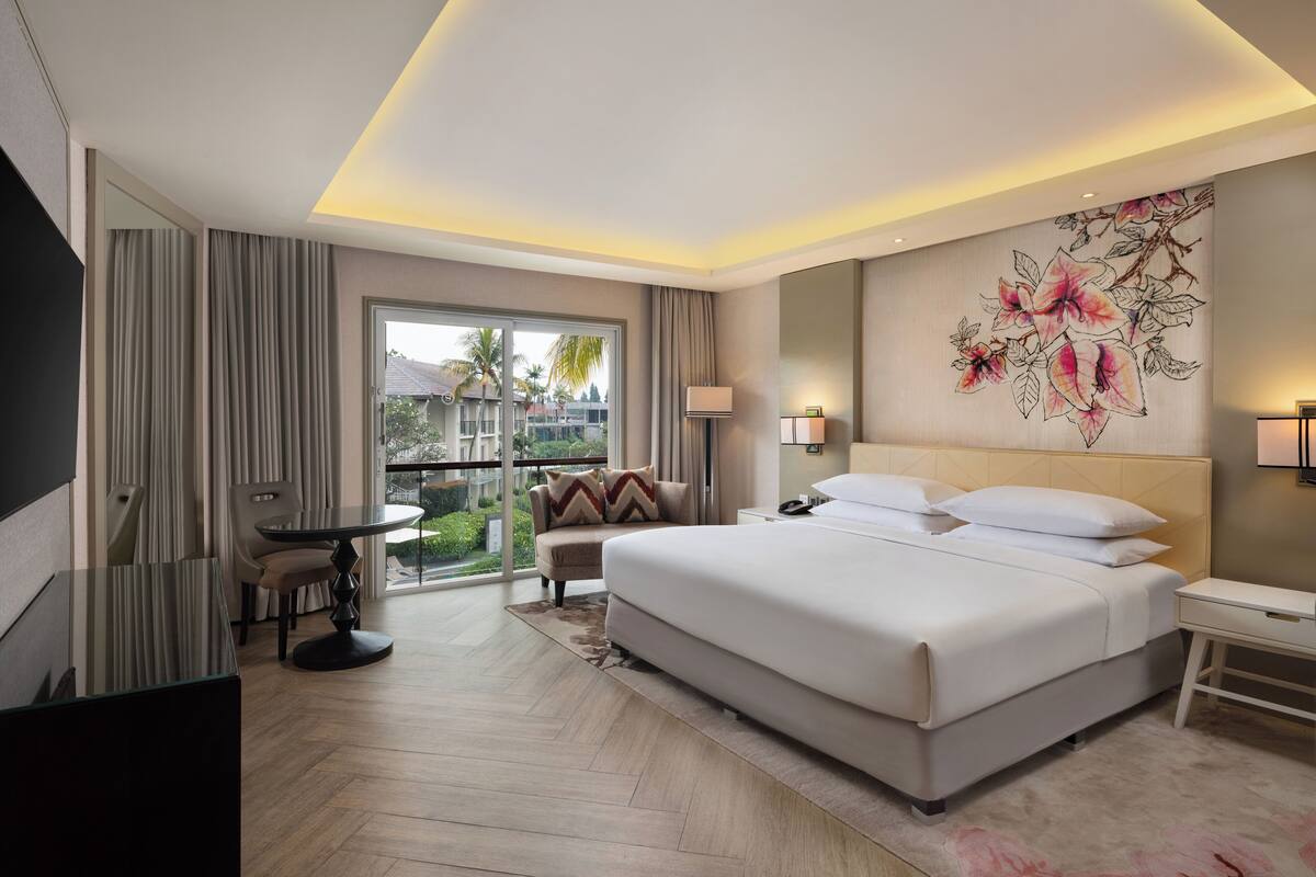 Une chambre d’hôtel moderne dotée d’un grand lit, d’un bureau, d’une chaise et d’un balcon offrant une vue sur les palmiers.
