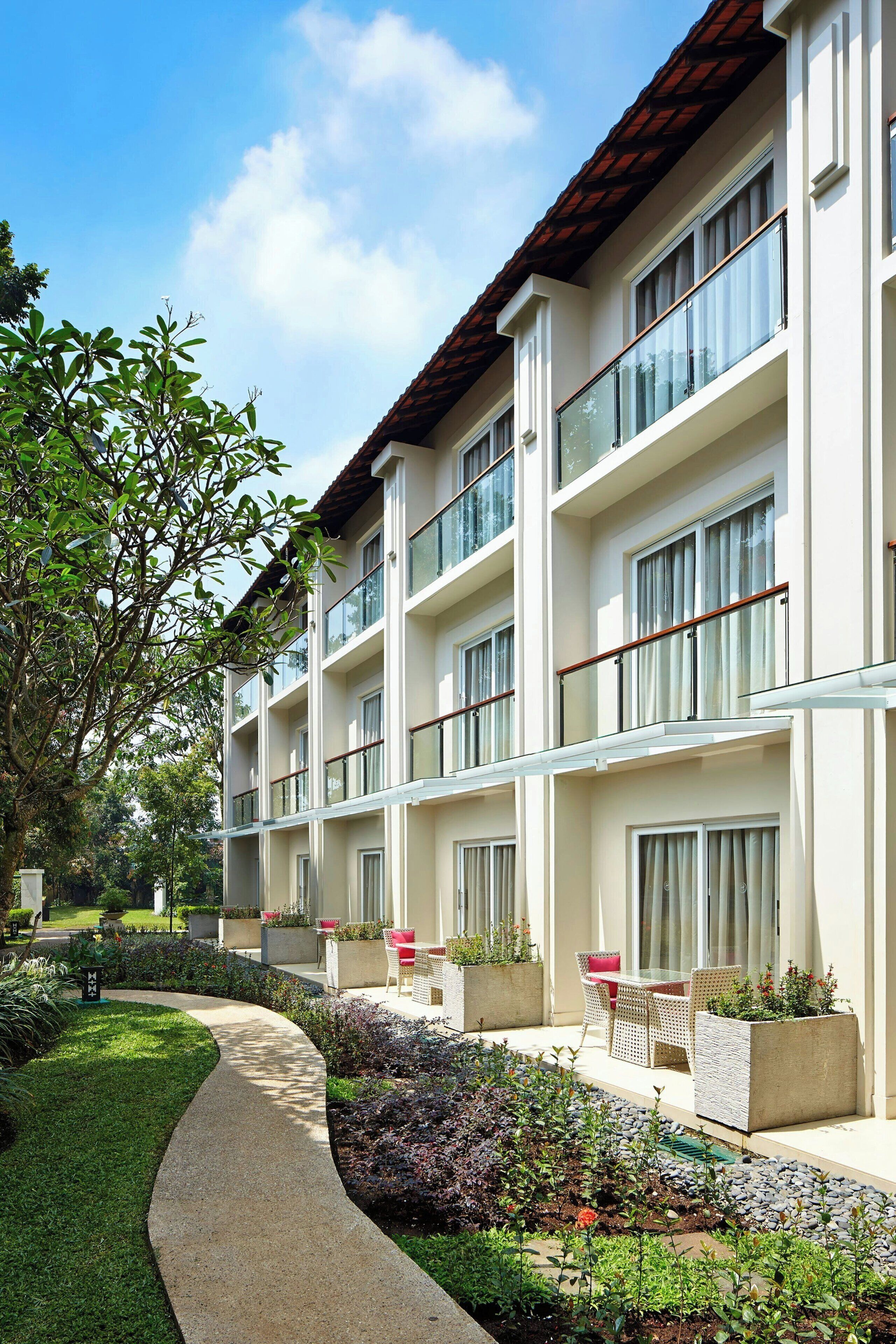 A multi-story hotel with balconies, outdoor seating, and a landscaped garden.