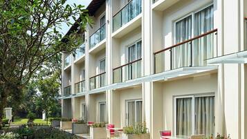 Un hotel de varios pisos con balcones, mobiliario exterior y un jardín ajardinado.