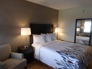 A hotel room with a bed, two bedside lamps, a nightstand, a chair, and a large mirror. - Red Roof Inn Somerset, PA (Somerset)