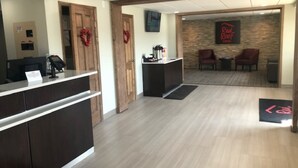 A reception area with a wooden reception desk, a coffee station, and a seating area with two chairs. - Red Roof Inn Somerset, PA (Somerset)