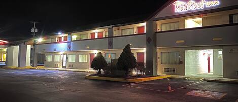 Un motel con un letrero de neón, varios pisos y un estacionamiento.