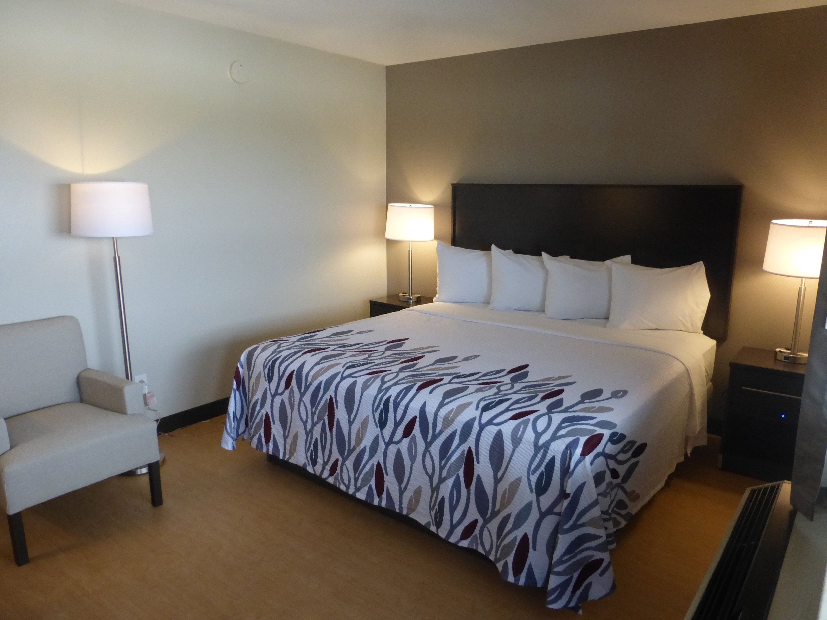 Une chambre d’hôtel avec un grand lit, deux tables de chevet avec des lampes, une chaise et une horloge murale.
