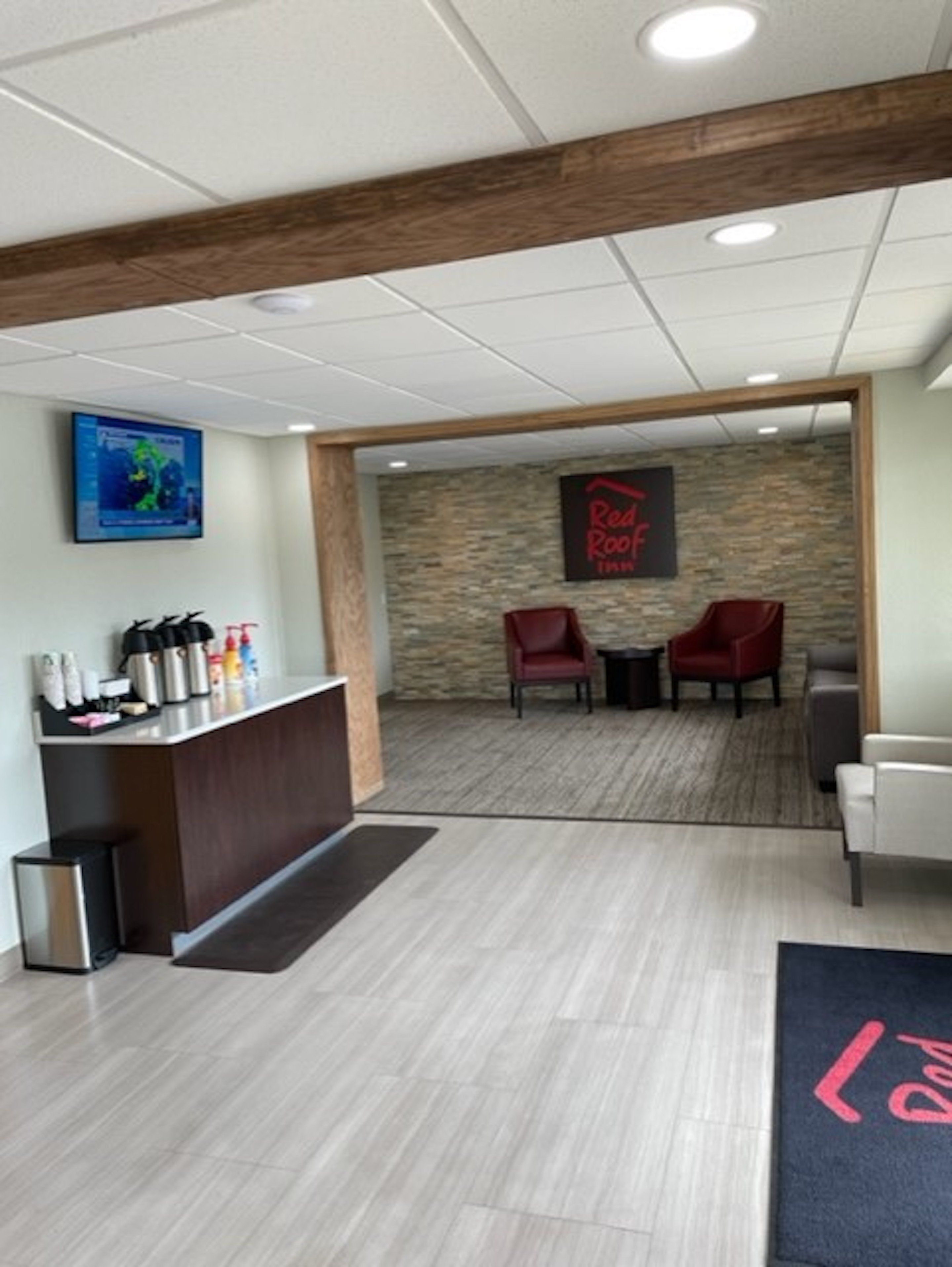 Un espace d’accueil avec un comptoir en bois, deux chaises rouges, un mur en pierre et une enseigne « Red Roof ».