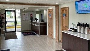 A hotel reception area with a wooden reception desk, a digital screen, and a view of the outside. - Red Roof Inn Somerset, PA (Somerset)