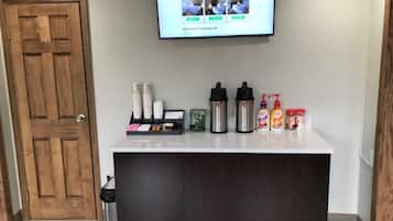 Una recepción con un televisor de pantalla plana mostrando el sitio web de Red Roof Inn, una cafetera, un dispensador de agua y una pequeña selección de artículos de aseo.