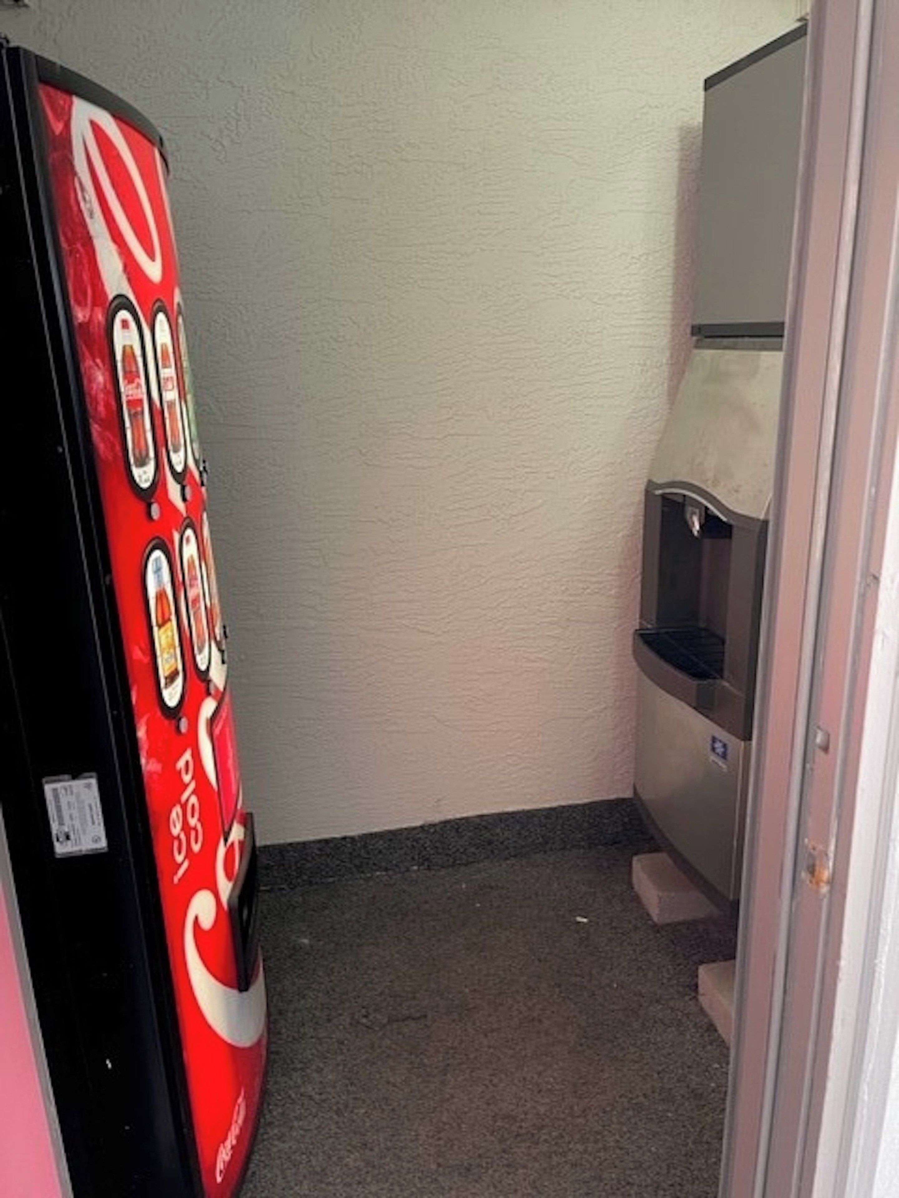 A narrow hallway with a vending machine on the left and a trash bin on the right.