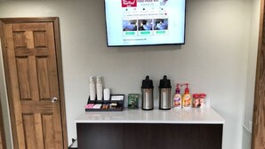 A reception area with a wooden door, a flat-screen TV displaying a Red Roof Inn website, and a counter with amenities like bottles and a box. - Red Roof Inn Somerset, PA (Somerset)