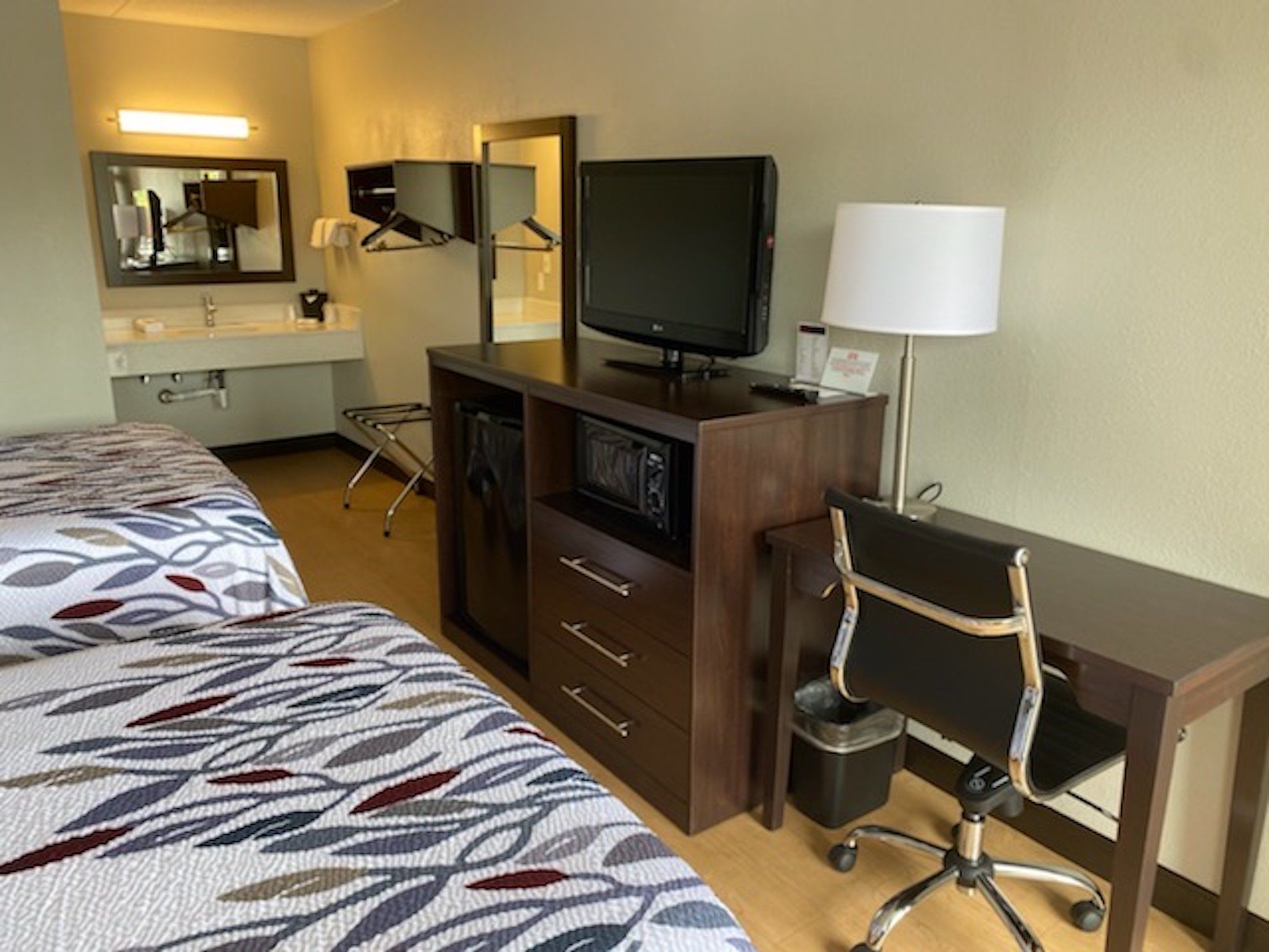 A hotel room with two beds, a desk with a chair, a television, and a lamp.