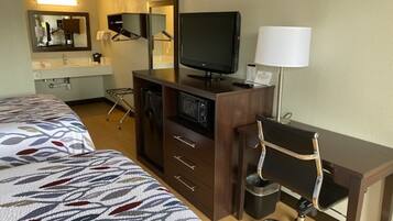 A hotel room with two beds, a desk with a chair, a television, and a lamp.