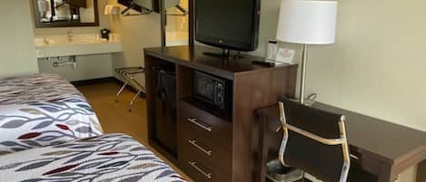 A hotel room with two beds, a desk with a chair, a television, and a lamp.