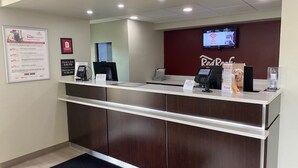 A reception desk with a digital screen, a phone, and a water dispenser. There is a sign on the wall and a mat with the hotel's name. - Red Roof Inn Somerset, PA (Somerset)