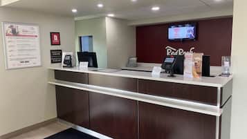 A reception desk with a digital screen, a phone, and a water dispenser. There is a sign on the wall and a mat with the hotel's name.