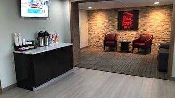 A reception area with a counter, a television, a Red Roof Inn sign, and two leather chairs.